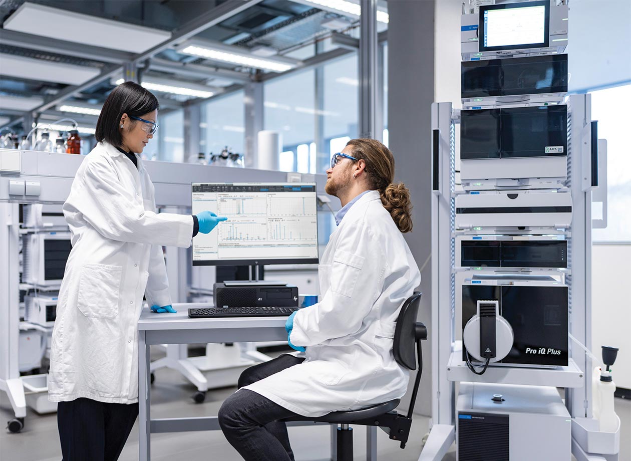 Two lab technicians discussing results on a computer monitor