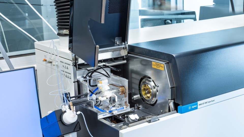 Open mass spectrometer in a laboratory setting, showing intricate tubes and components. The scene conveys a sense of precision and advanced technology.