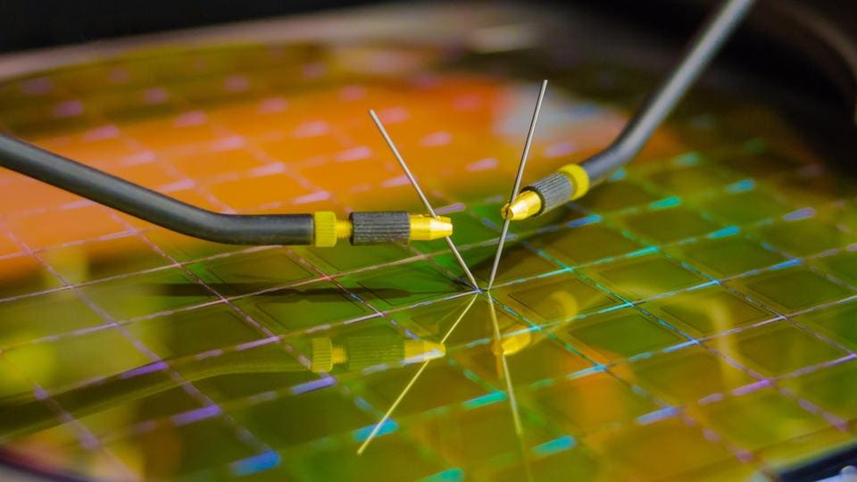 Close-up of a silicon wafer with microchip circuits, intersected by two delicate probe needles for testing.